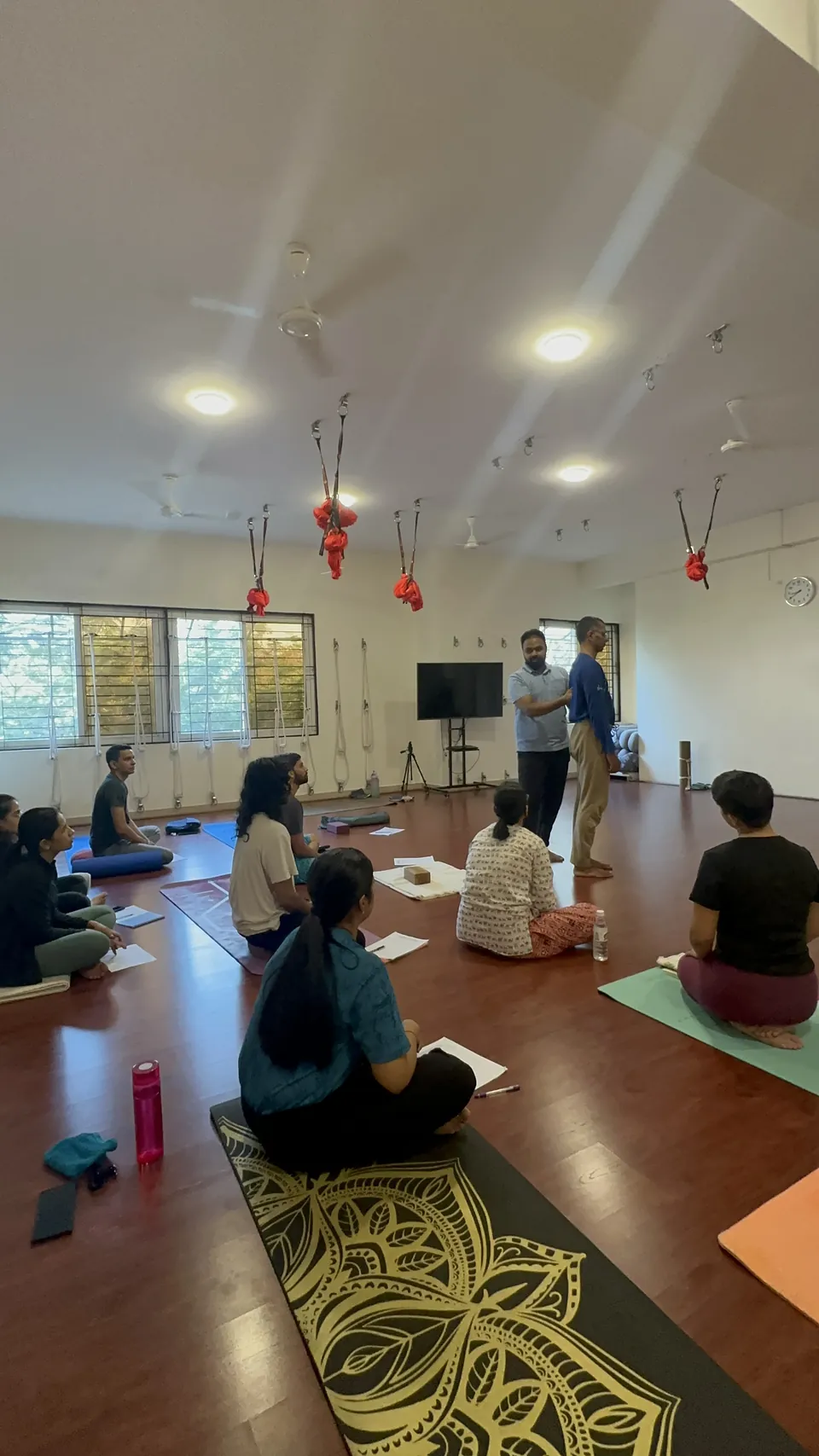 A study session: participants seated on mats with handouts while the teacher demonstrates at the front of the hall