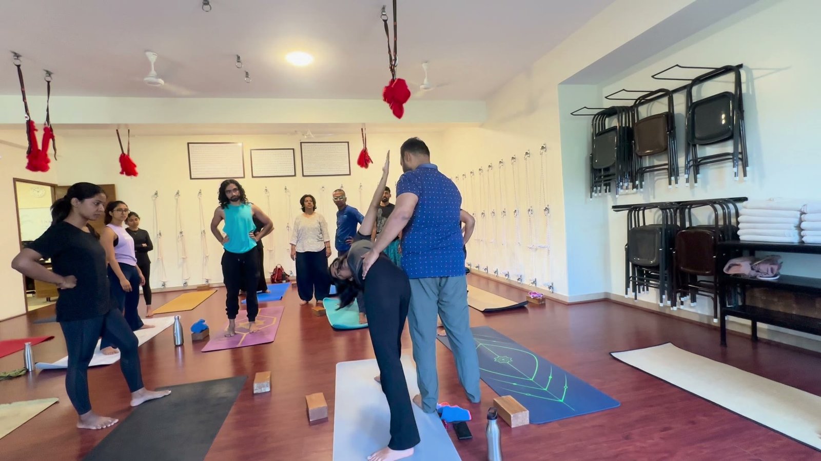 A teacher works with one student in the middle of the hall while the rest of the class stands on their mats watching.