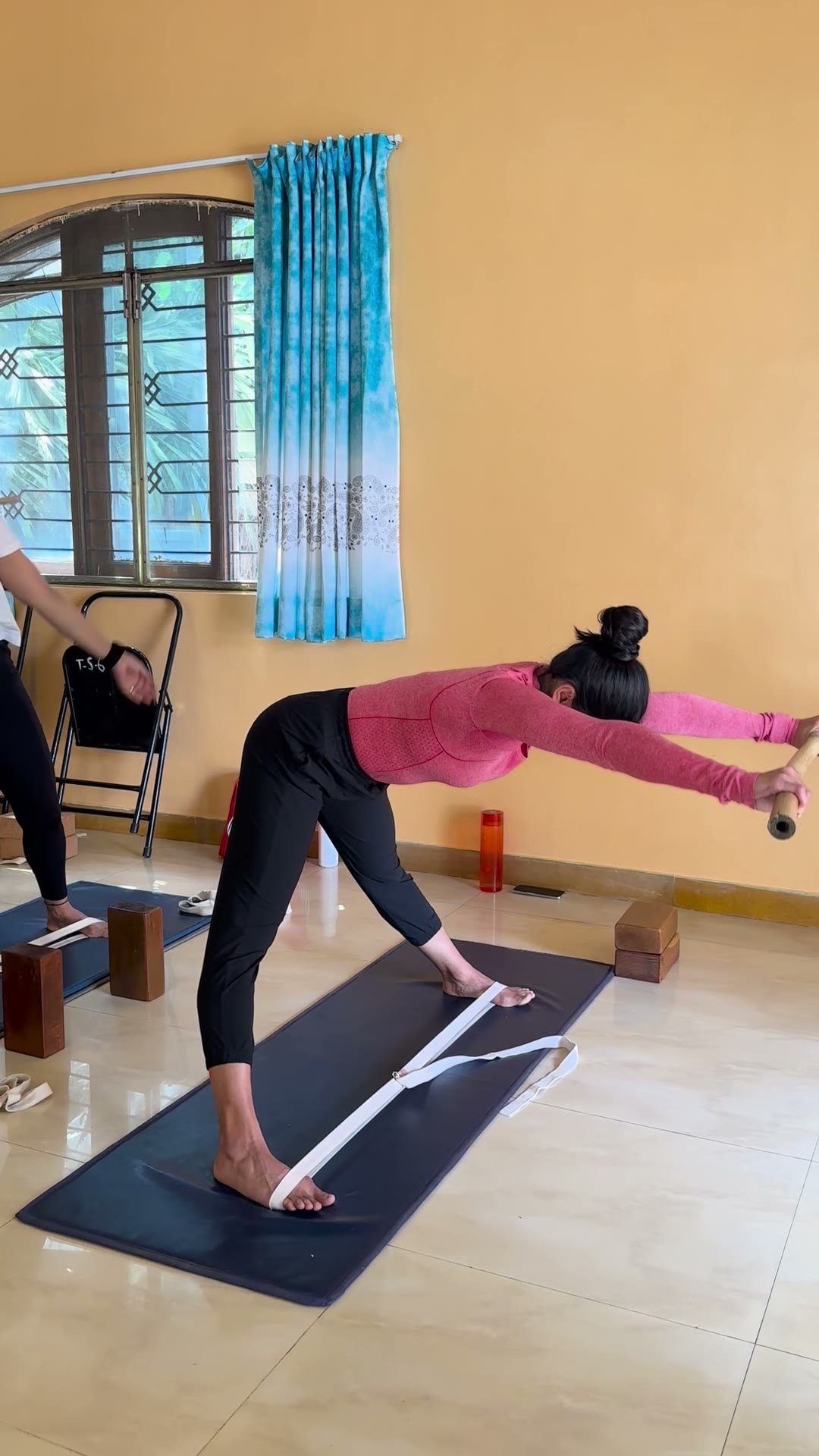 A woman folding forward on her mat with a dowel, then rising to standing