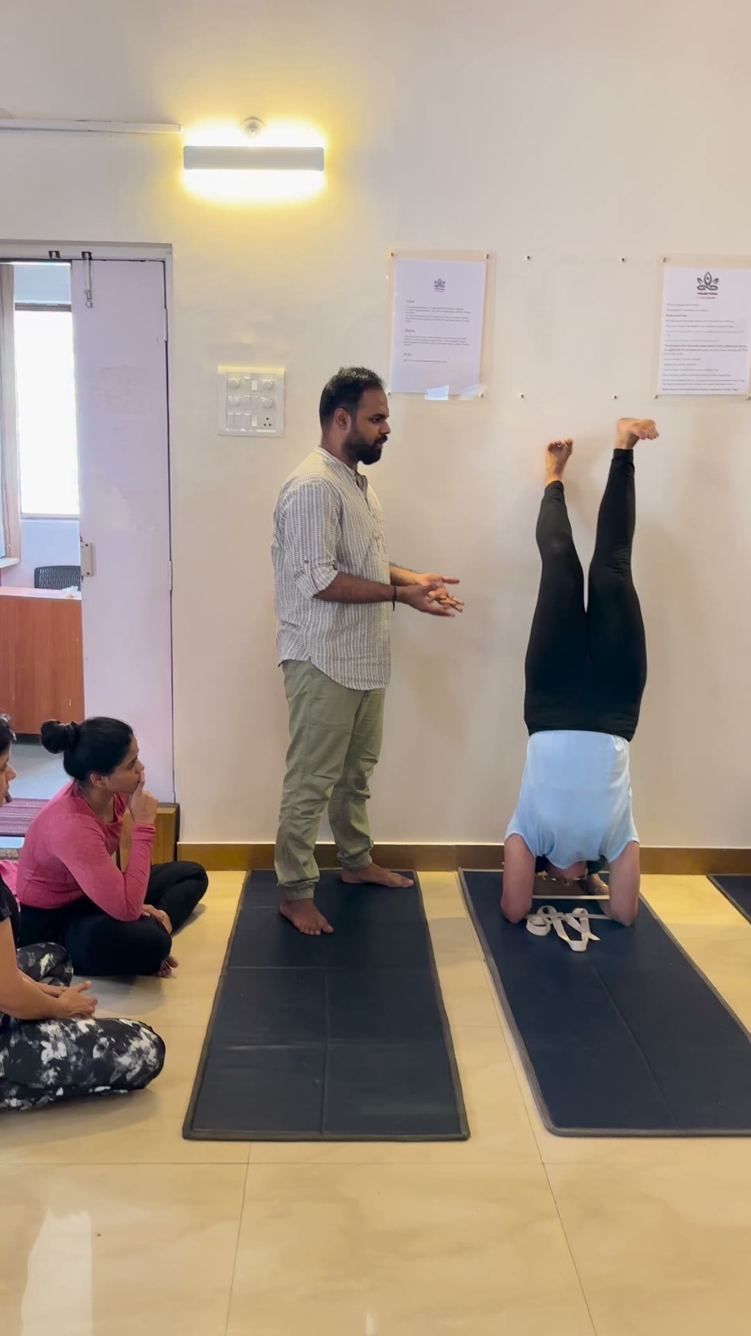 A teacher supporting a student in an inversion against the wall, then helping her down