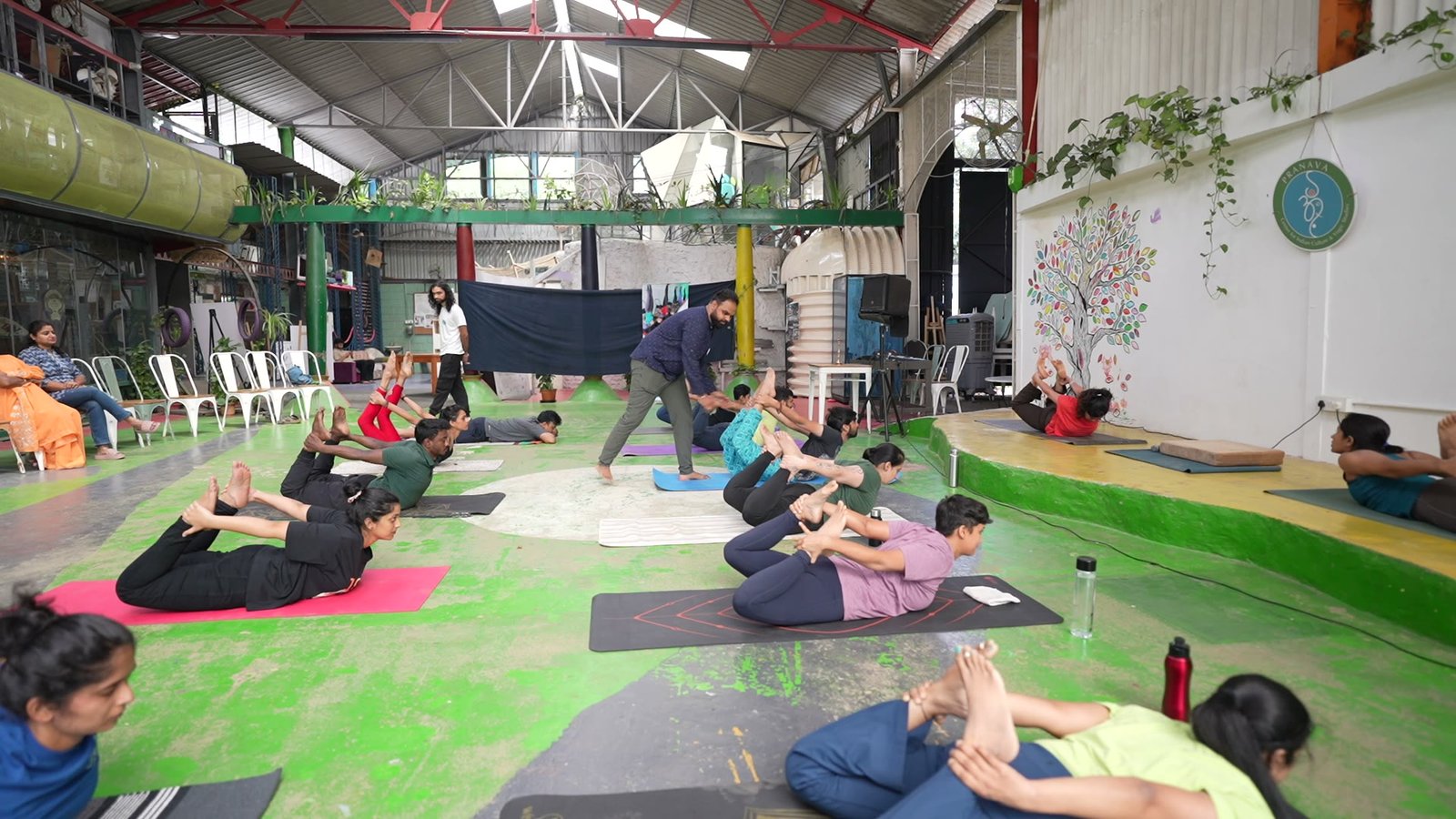 A teacher moving among students seated on their mats across the open hall floor.