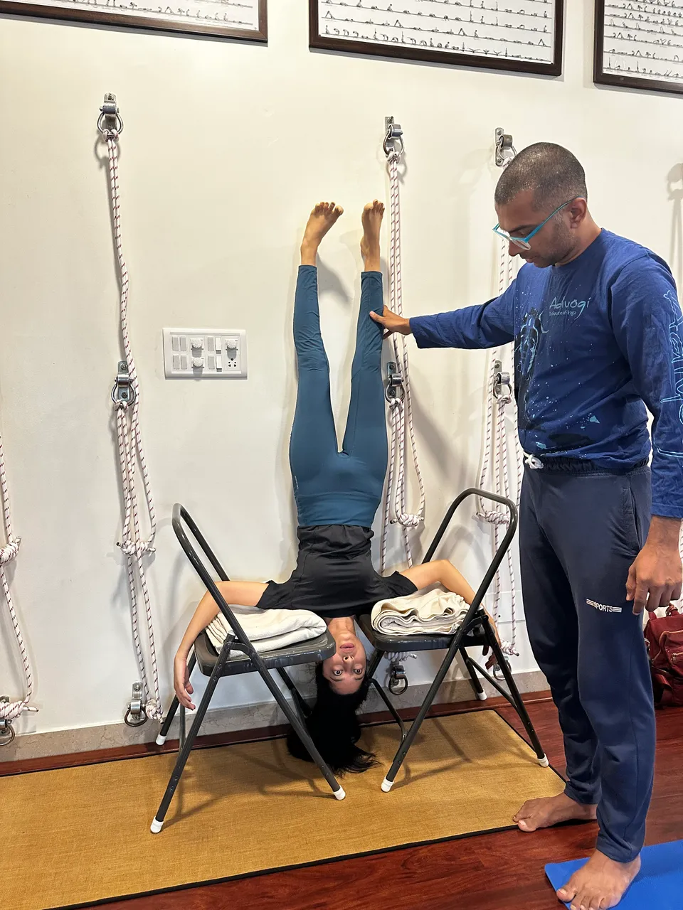 Teacher guiding a student's legs during a chair-supported inversion in a studio