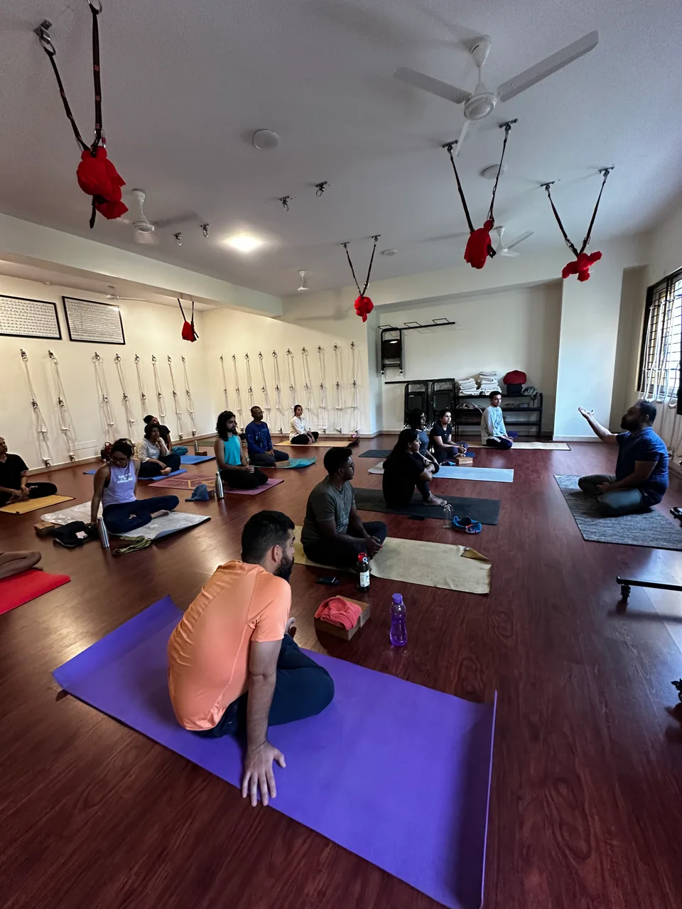 A participant sitting back on her heels on a purple mat in the foreground of a class, the rest of the group seated behind her.