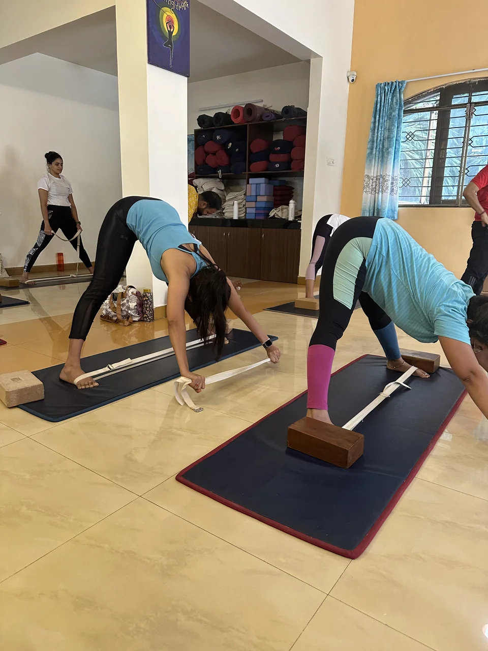 A woman folding forward with her foot on a wooden block and a stick laid along the mat