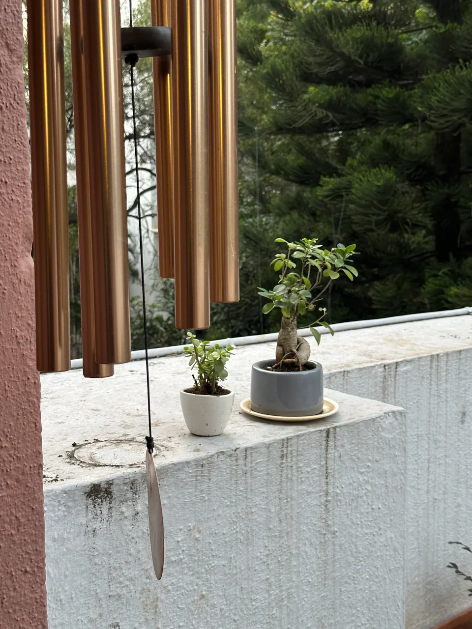 Brass wind chime tubes hanging beside a pillar above a white parapet with two potted plants