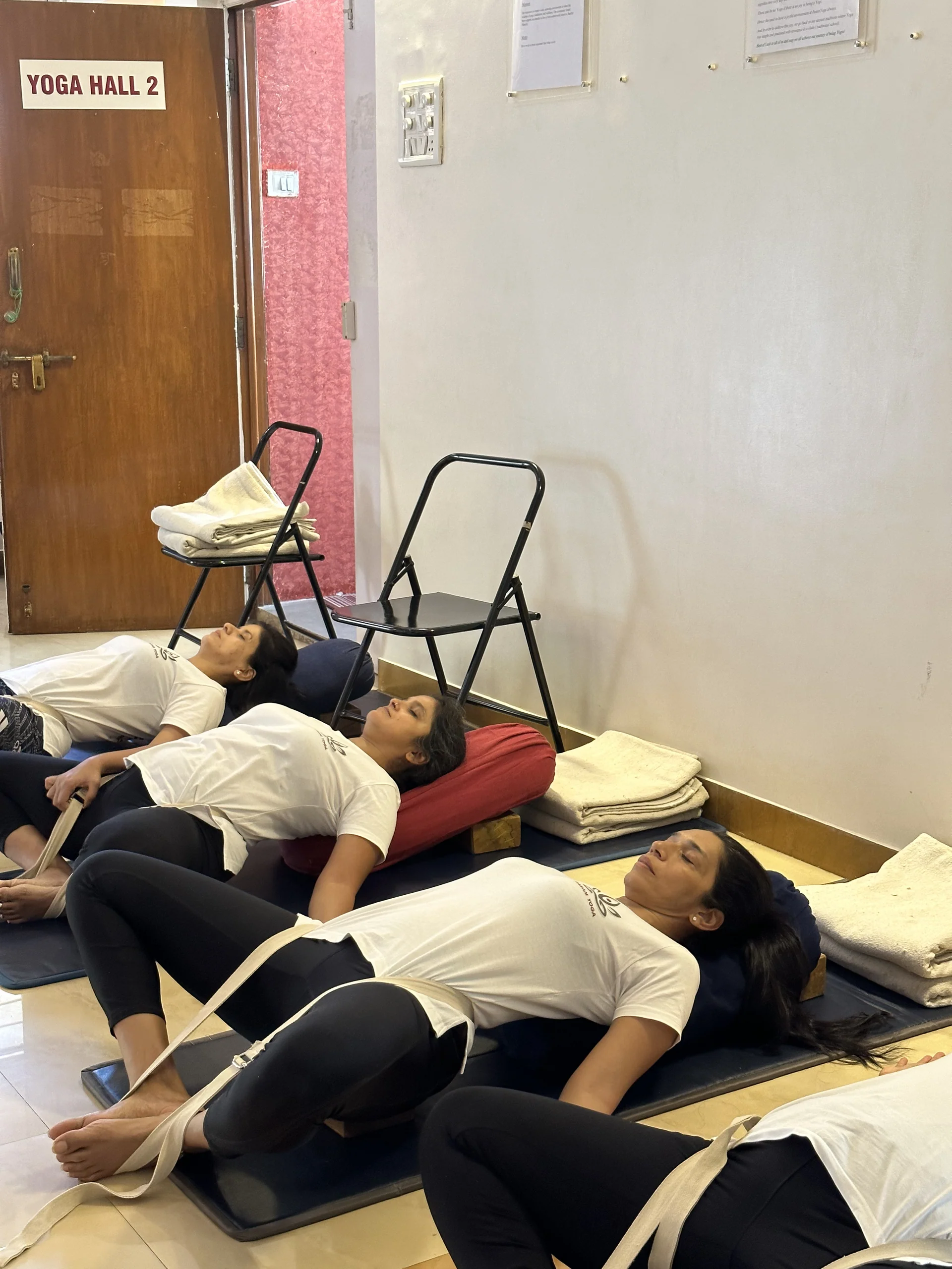 Three women lying in a row with knees open, belts around their feet and bolsters under their heads
