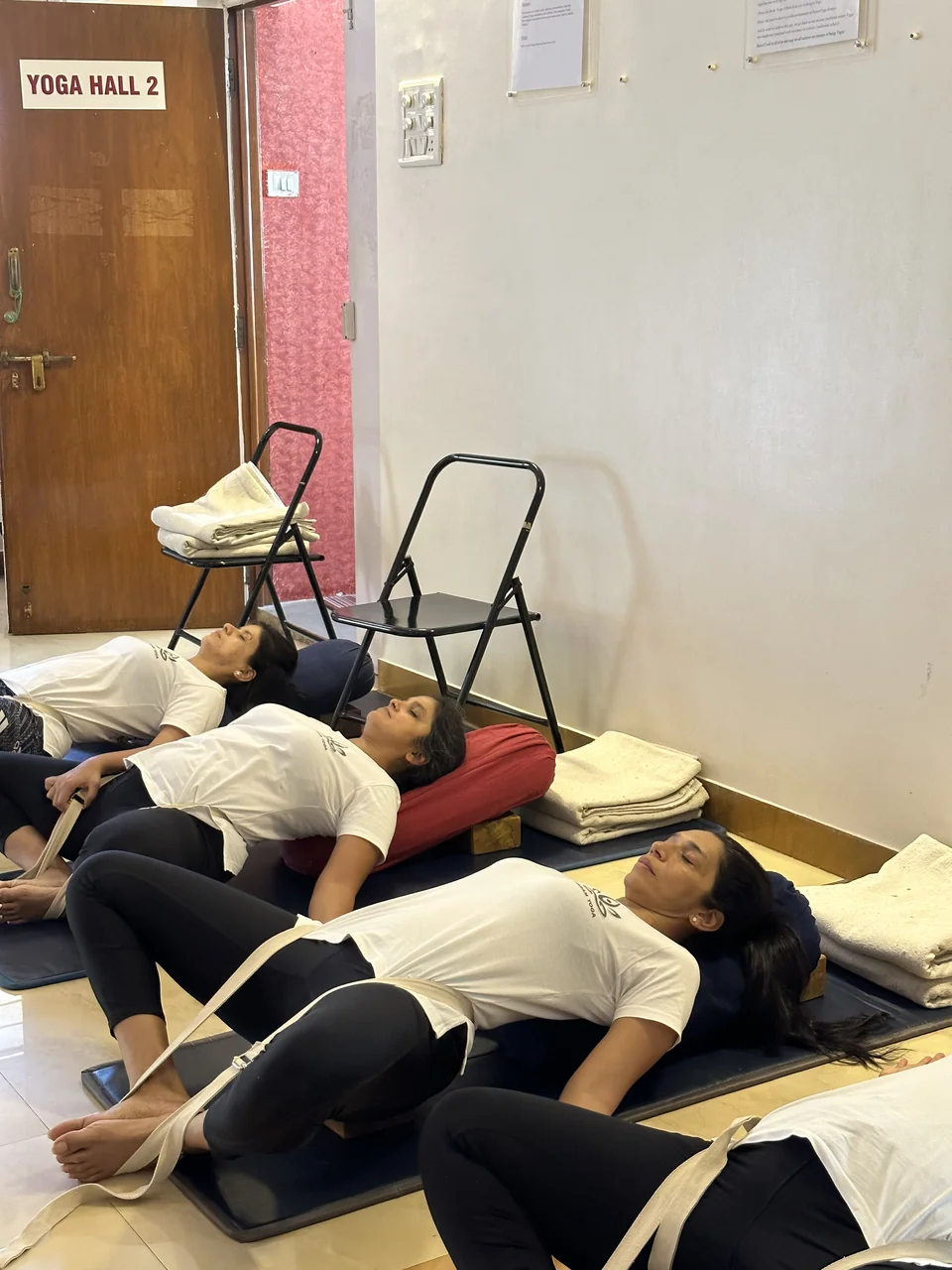 Three women resting in a supported restorative pose on bolsters and belts