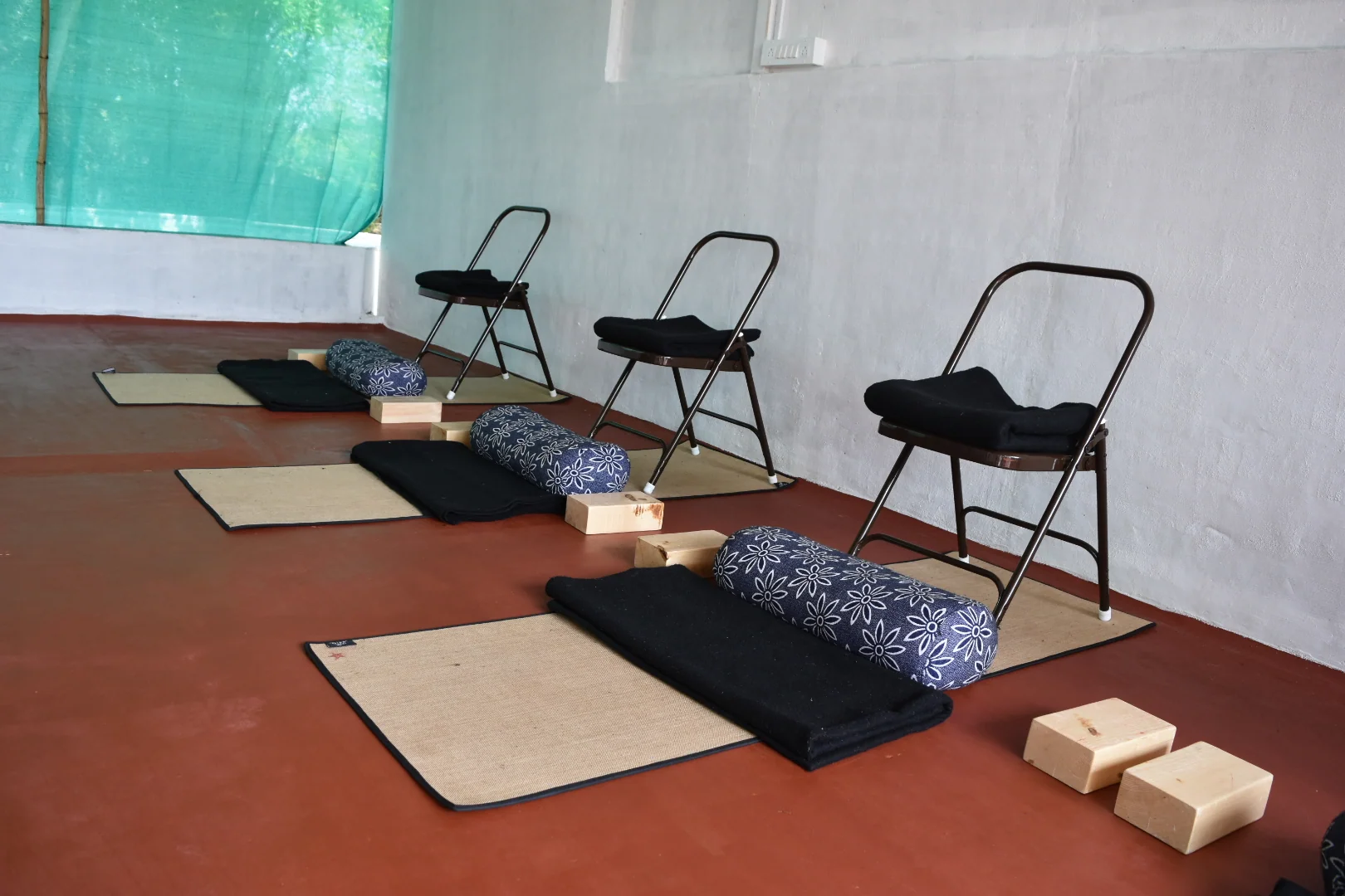 An empty row of folding chairs, mats, blankets, bolsters and wooden blocks on a red floor