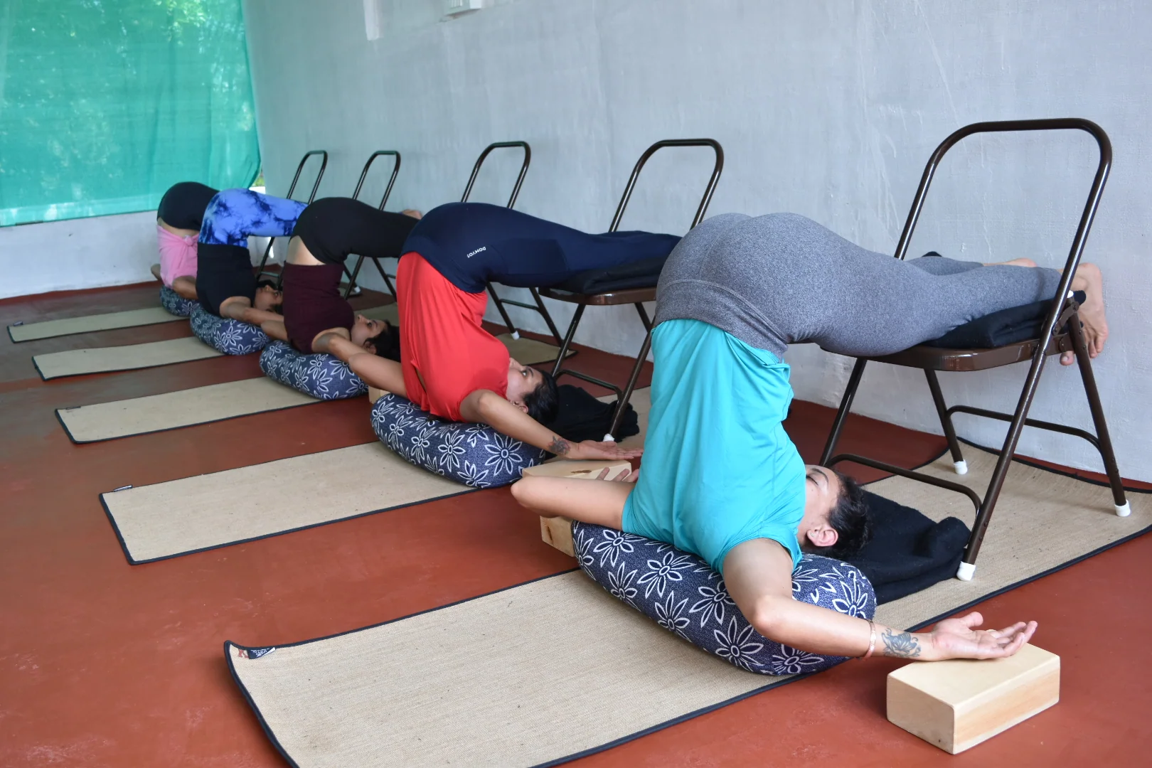 Four practitioners lying back over bolsters with their legs resting on chair seats