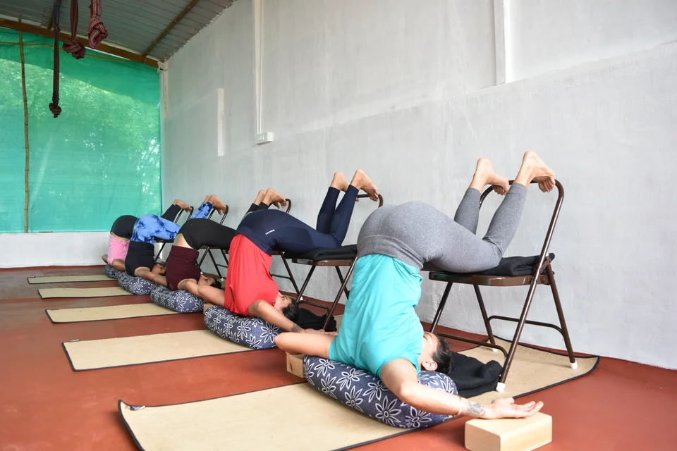 Four practitioners in supported bridge over chairs with a rope hanging from the roof beam