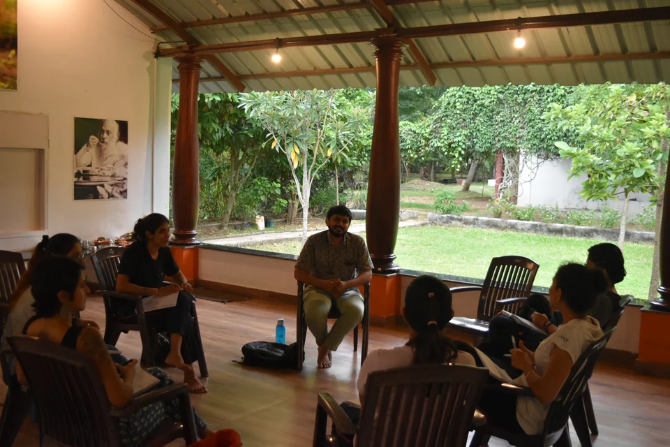 A discussion circle of people on chairs in an open pavilion, one man leaning forward speaking