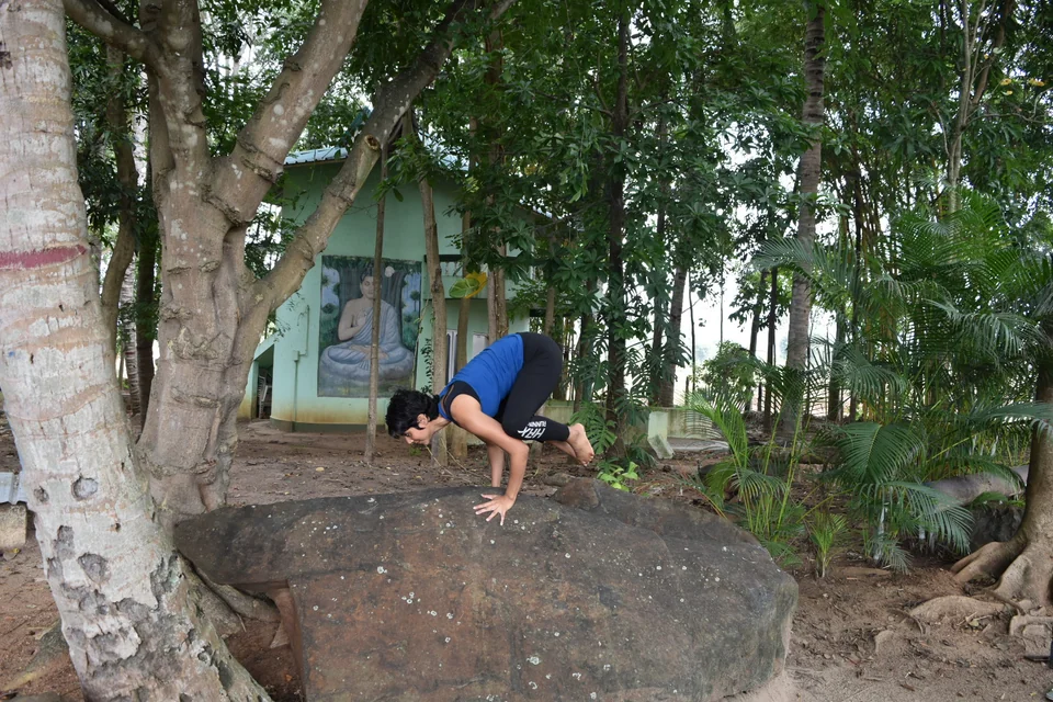A woman balancing on her hands on a large boulder among trees