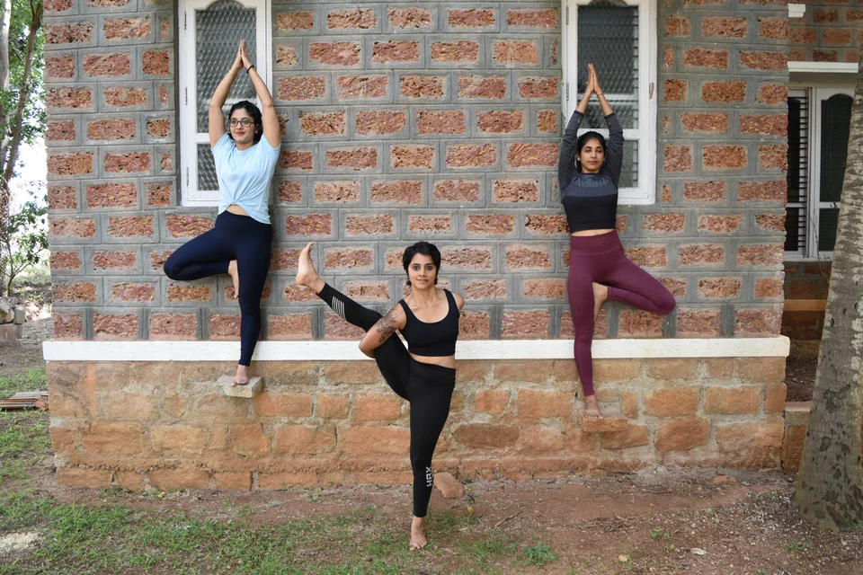 Three women holding balancing poses against an exposed brick wall