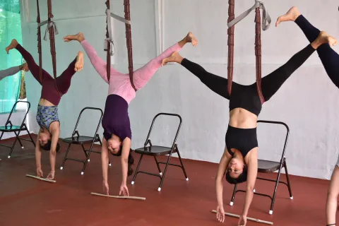 Three women hanging inverted from wall ropes with legs spread wide, hands on the floor