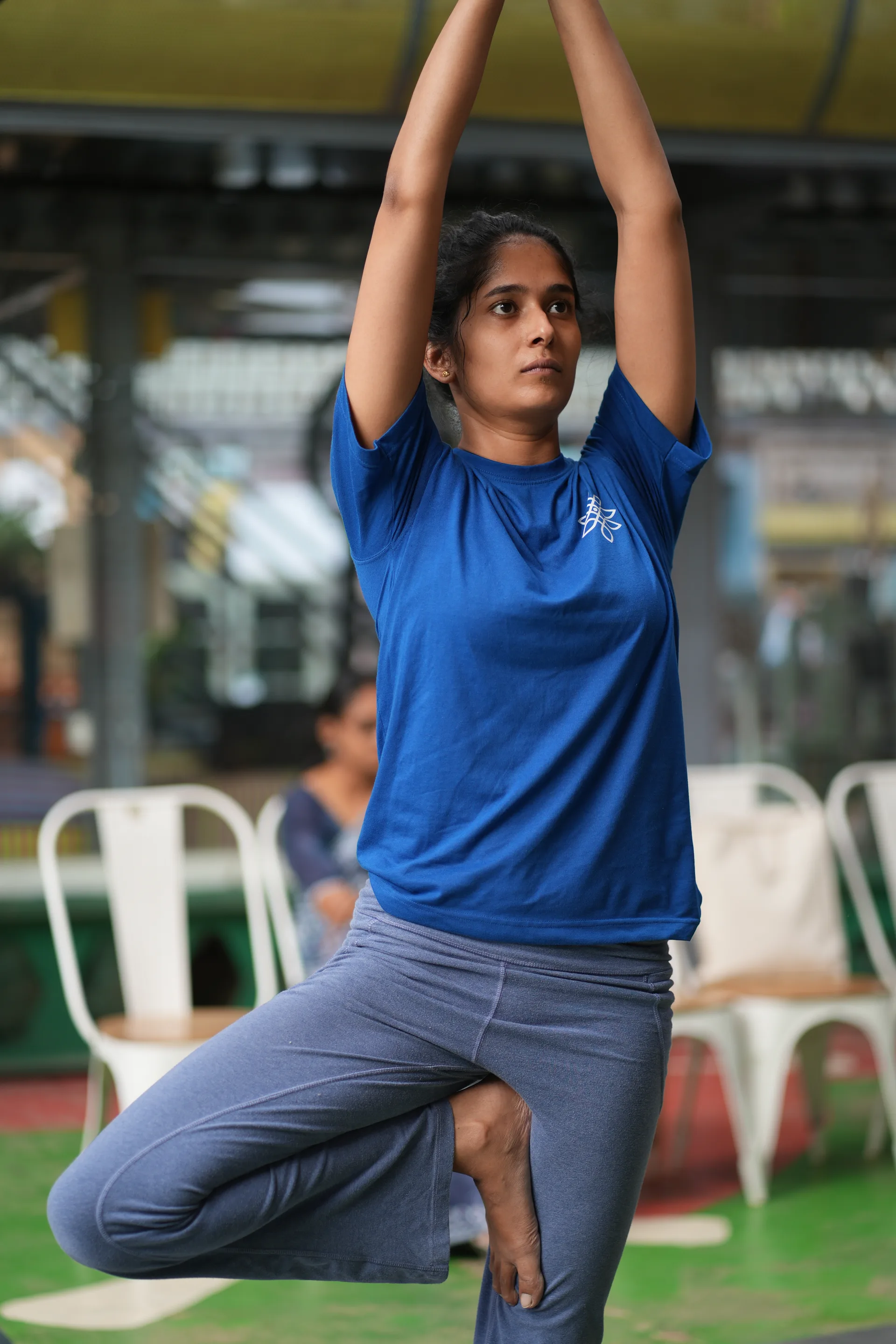 A practitioner balances on one leg with both arms lifted overhead in an outdoor class.