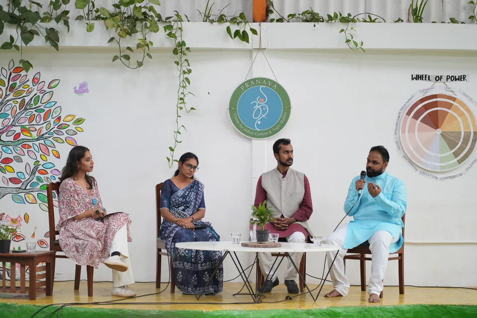 Four panellists on wooden chairs on a green stage, talking together.
