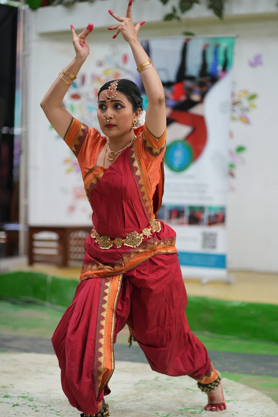 A Bharatanatyam dancer in a low stance with both arms raised in a mudra
